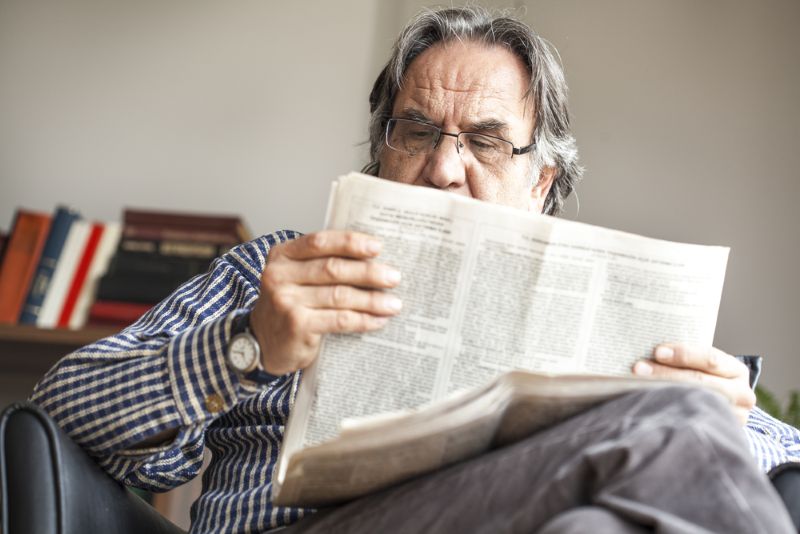 old man in his living room reading a newspaper