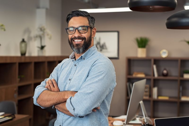 Man standing in office with arms crossed smiling