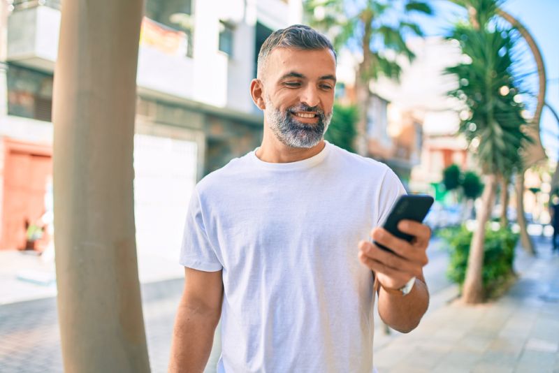 Middle aged Hispanic man walking outside and smiling at phone